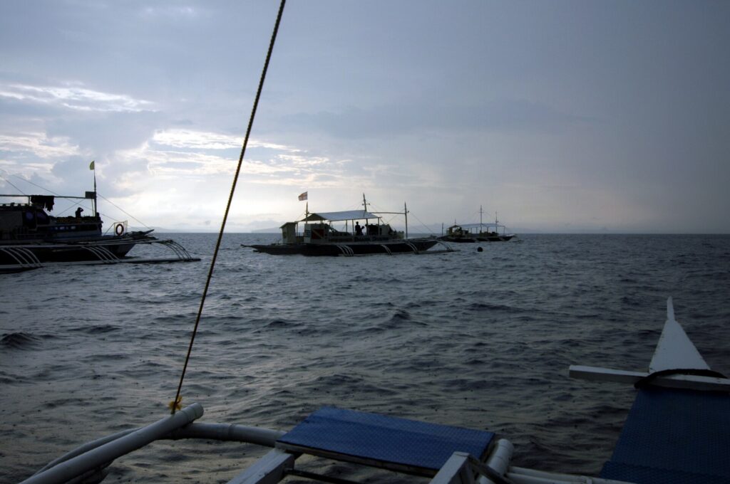 Três bancas de mergulho ancoradas em Monad Shoal sob um céu cinza de manhã cedo, vistas do convés de outro barco