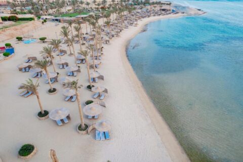 Vista aérea da praia do Blend Elphistone Resort, com palmeiras, guarda-sóis de palha e o mar turquesa