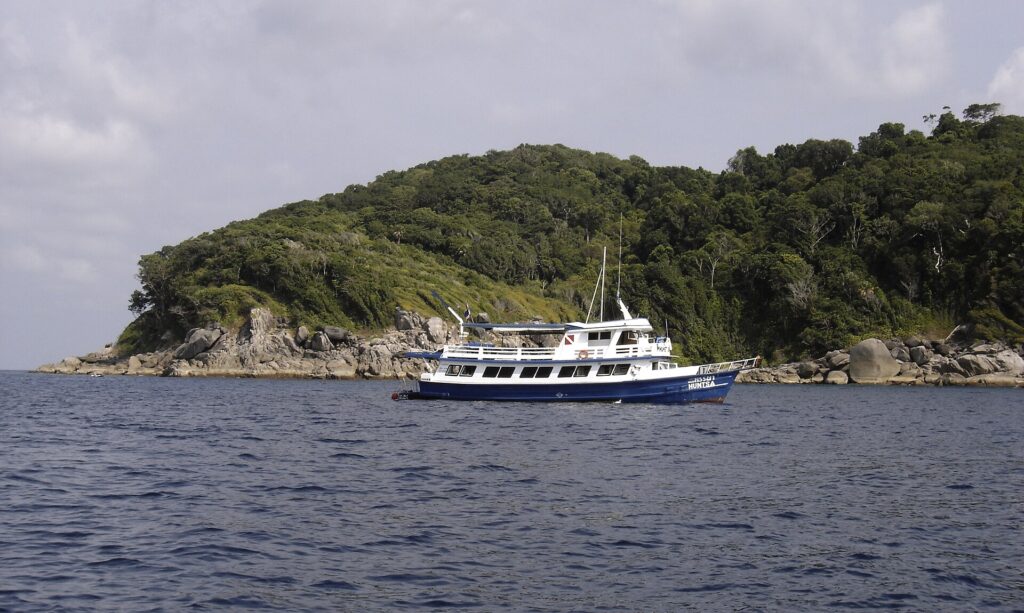 Um barco de cruzeiro azul e branco ancorado diante de uma ilha das Similan, com seus blocos de granito cinza rente à água sob a floresta