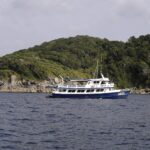 Um barco de cruzeiro azul e branco ancorado diante de uma ilha das Similan, com seus blocos de granito cinza rente à água sob a floresta