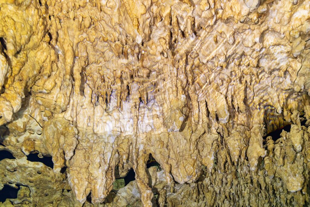 Close de formações amarelo-claras e estalactites finas, com o reflexo ondulado da água embaixo