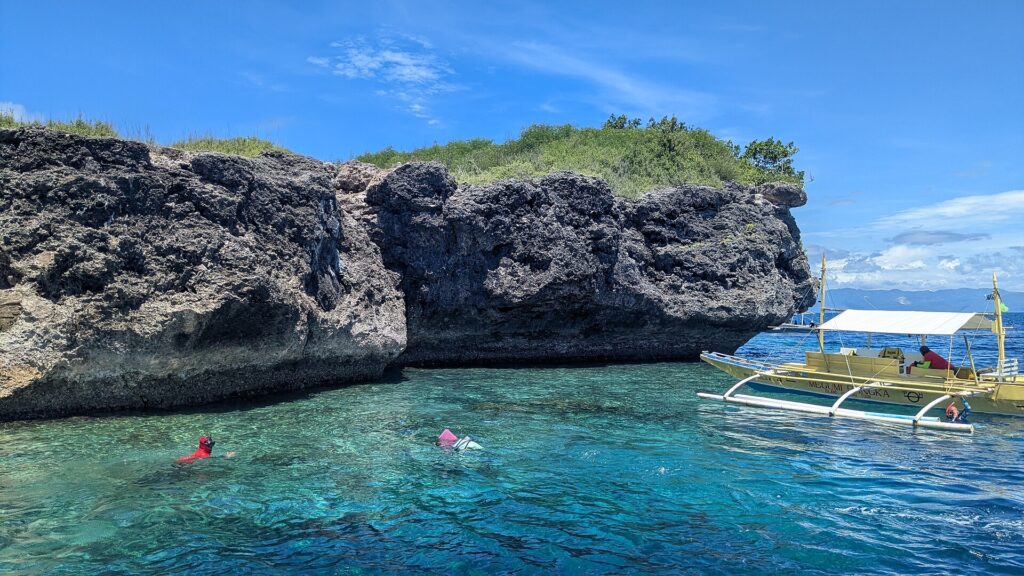 A falésia de calcário cinza e escavada da ilha de Pescador, dois nadadores com máscara e snorkel e uma banca amarela em água turquesa