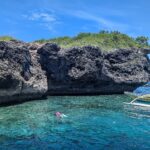 A falésia de calcário cinza e escavada da ilha de Pescador, dois nadadores com máscara e snorkel e uma banca amarela em água turquesa