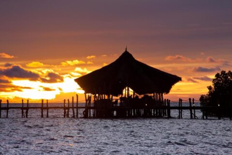 O pavilhão com telhado de palha do Fundu Lagoon, sobre palafitas no fim do píer, ao pôr do sol