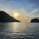 A Ilha do Coco contra a luz ao pôr do sol, com um barco de cruzeiro ancorado à direita e o mar calmo