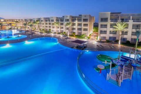 As piscinas iluminadas do JAZ Soma Beach ao anoitecer, entre os prédios e as palmeiras