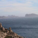 Das rochas calcárias do Frioul, em primeiro plano, vista de um mar agitado e cheio de espuma até a ilha Maïre e a costa de Les Goudes, recortadas na bruma.