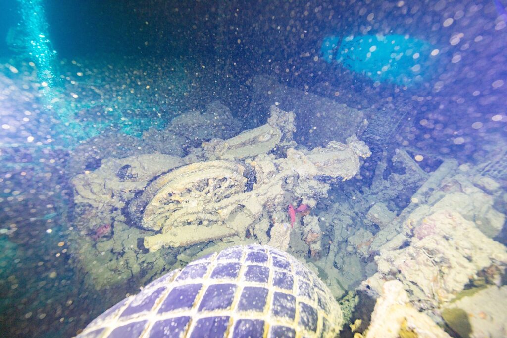Num porão escuro do Thistlegorm, uma moto tombada atrás de um pneu de caminhão, iluminada pela lanterna