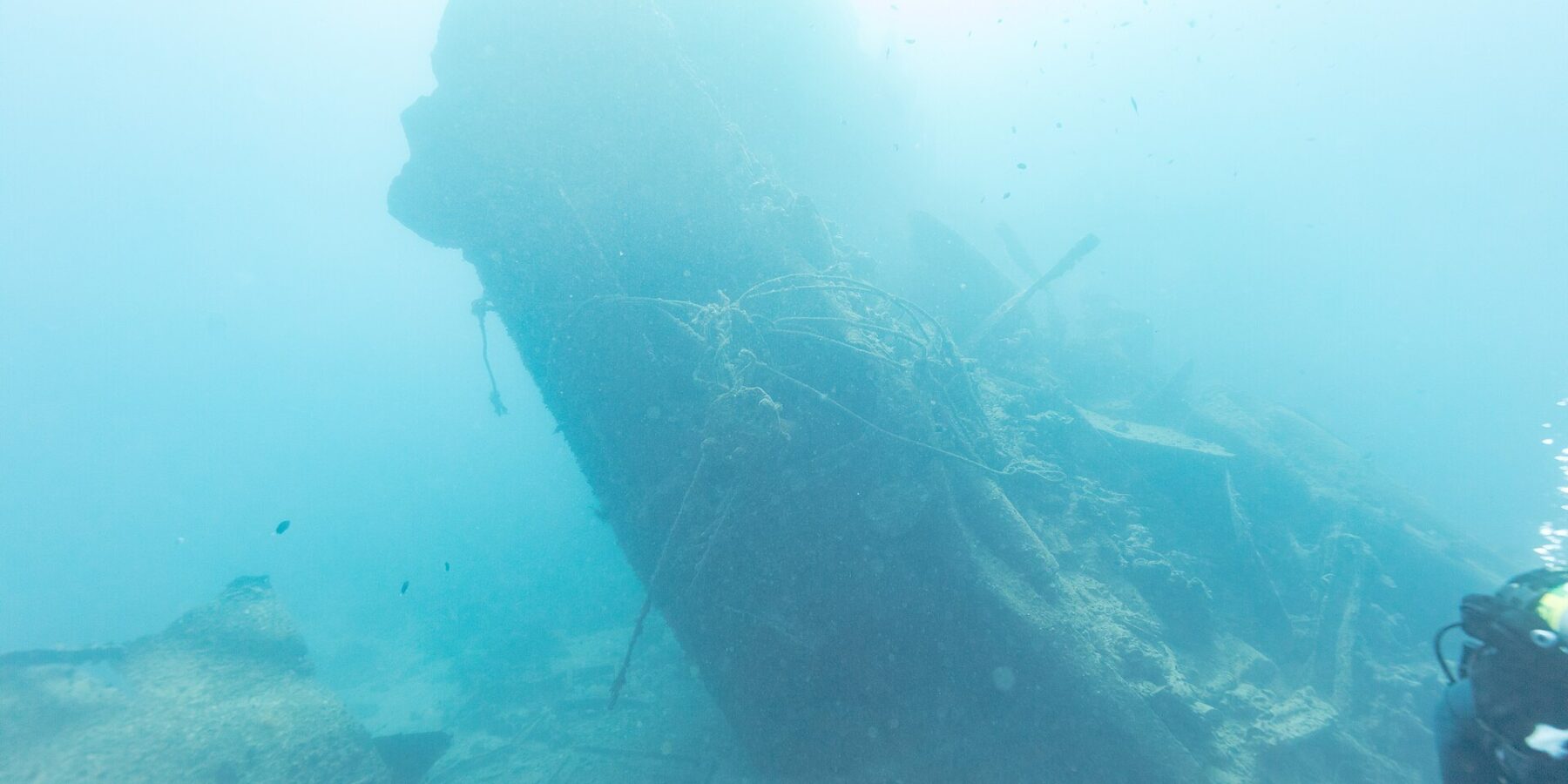 A popa partida do Thistlegorm, erguida e inclinada no azul, com um mergulhador à direita