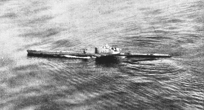 Foto de arquivo em preto e branco, tirada de um avião, de um submarino navegando na superfície de um mar encrespado, com a esteira ao longo do casco e a torre no centro.