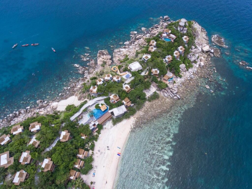 Vista aérea do Sai Daeng Resort, com bangalôs numa ponta de pedras, piscinas e praia de areia