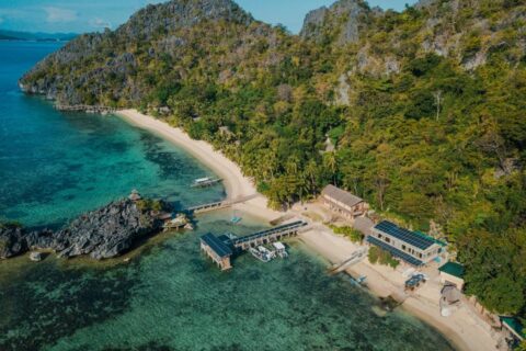 Vista aérea do Sangat Island Dive Resort, com a praia, o píer e os barcos, ao pé das falésias