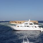 Três barcos de cruzeiro amarrados diante da ilhota plana de Small Brother, com o farol de Big Brother visível no horizonte