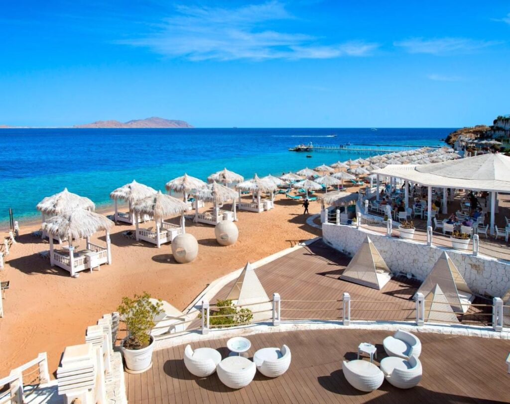 A praia do Sunrise Arabian Beach Resort, com guarda-sóis de palha e píer, de frente para a ilha de Tiran