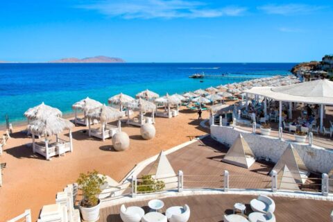 A praia do Sunrise Arabian Beach Resort, com guarda-sóis de palha e píer, de frente para a ilha de Tiran