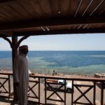 De um deque de madeira, um homem de galabia olha a piscina do Blue Hole, cercada de recife claro, onde nadam banhistas